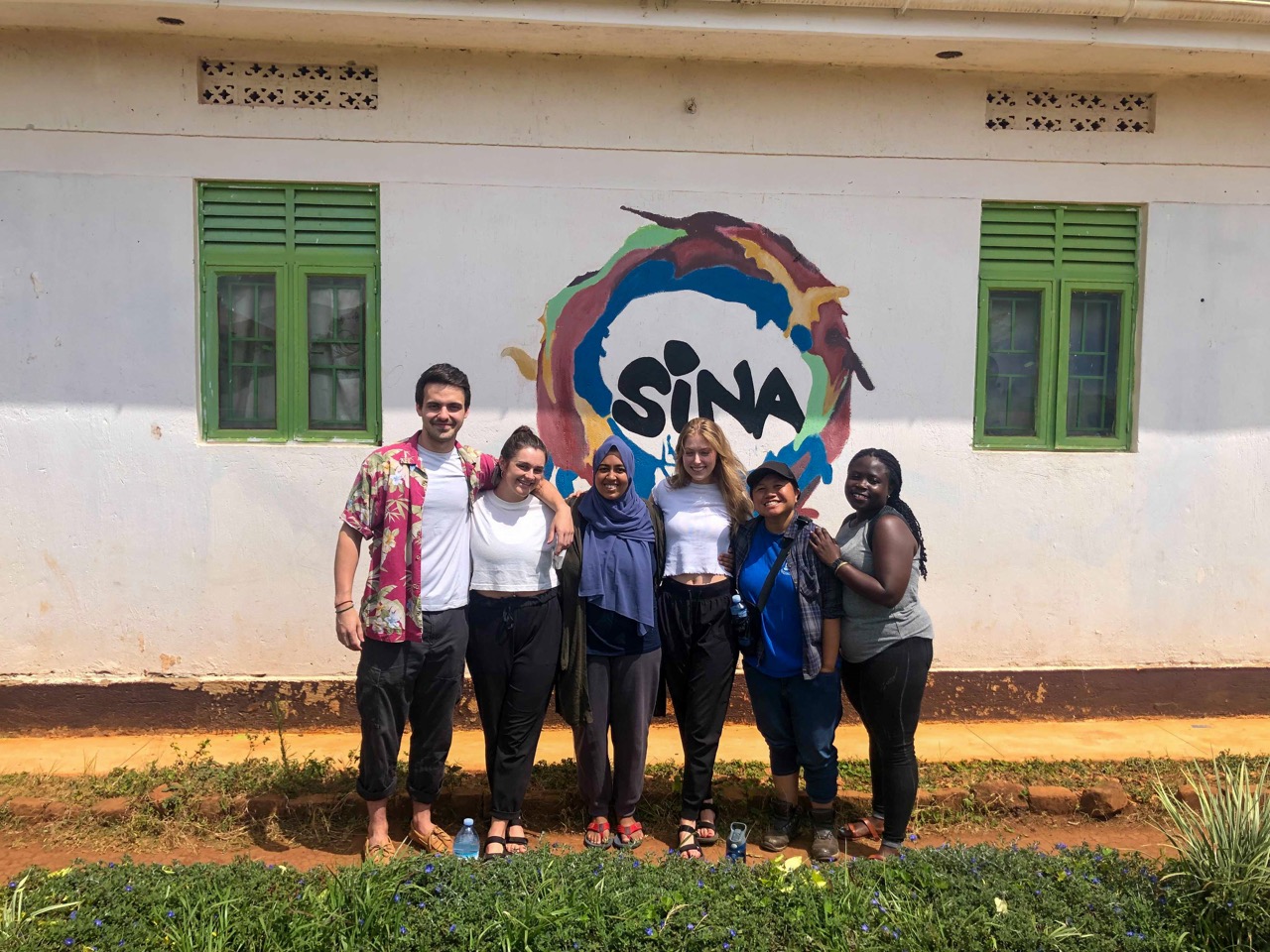 6 volunteers stand in front of a sign that reads SINA