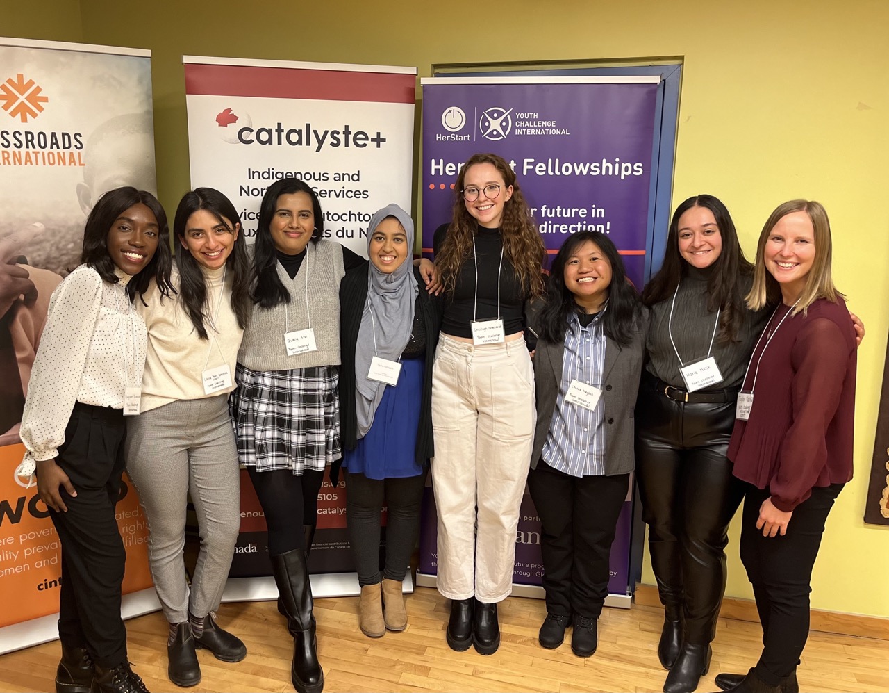 8 young women in front of organization promotional signs
