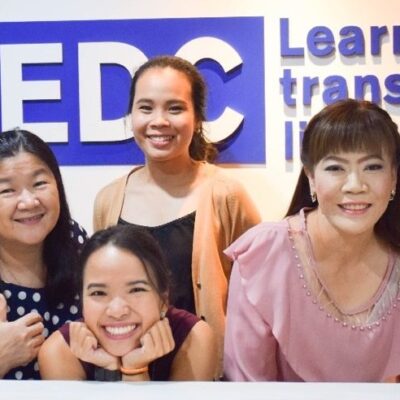Eight women smiling and posing together in front of an EDC Learning Transforming Lives sign.