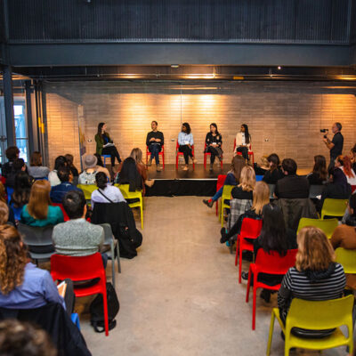 A panel discussion in progress with an audience seated and listening attentively in a modern event space.
