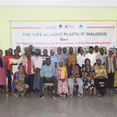 A group of people pose together at the "Life Without Plastics" dialogue event in front of a banner.