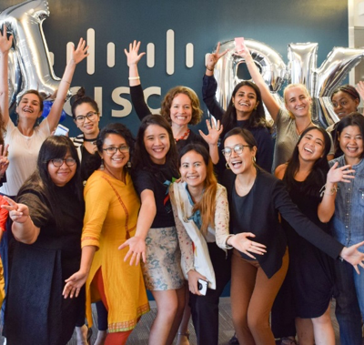 A group of people smiling and posing with balloons spelling "HOLIDAY" in an office setting.