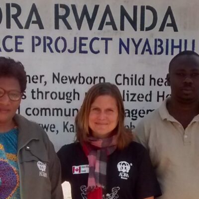 Five people stand in front of an "ADRA Rwanda Embrace Project Nyabihu" sign outdoors.