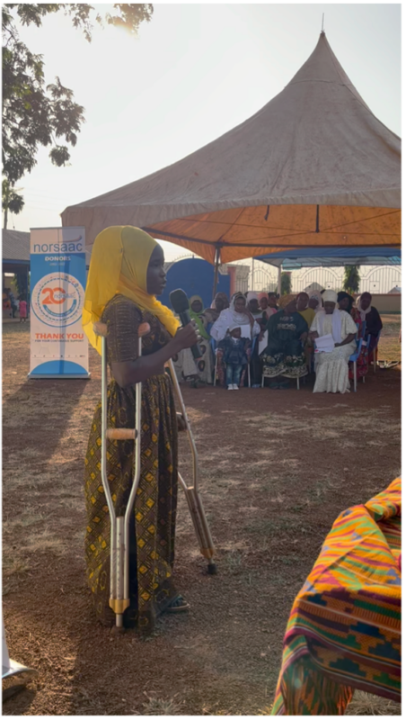 Supporting-economic-opportunities-for-women-with-disabilities-in-Ghana_3 A young woman on crutches speaks into a microphone at an outdoor event under a tent.