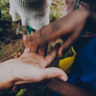 Several hands of different skin tones touching and holding each other outdoors, showing connection and unity.